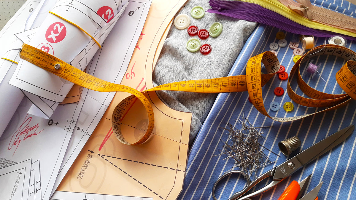 A photograph featuring various paper sewing patterns alongside sewing notions such as buttons, tailor scissors, pins, and measuring tape.