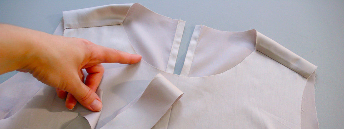 A hand indicating the unfinished neckline of a garment. 