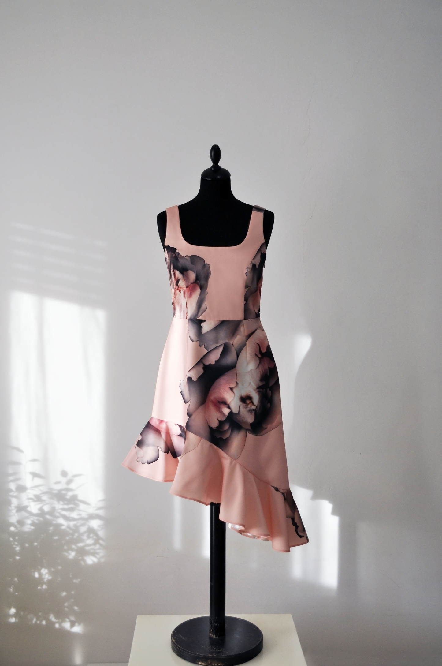 A flouncy pink dress with an asymmetrical hemline on a tailor mannequin.