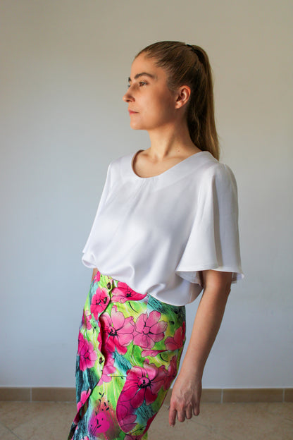 A woman with a ponytail hairstyle wears a white crepe satin blouse tucked into a floral front buttoned pencil skirt with large side pockets.