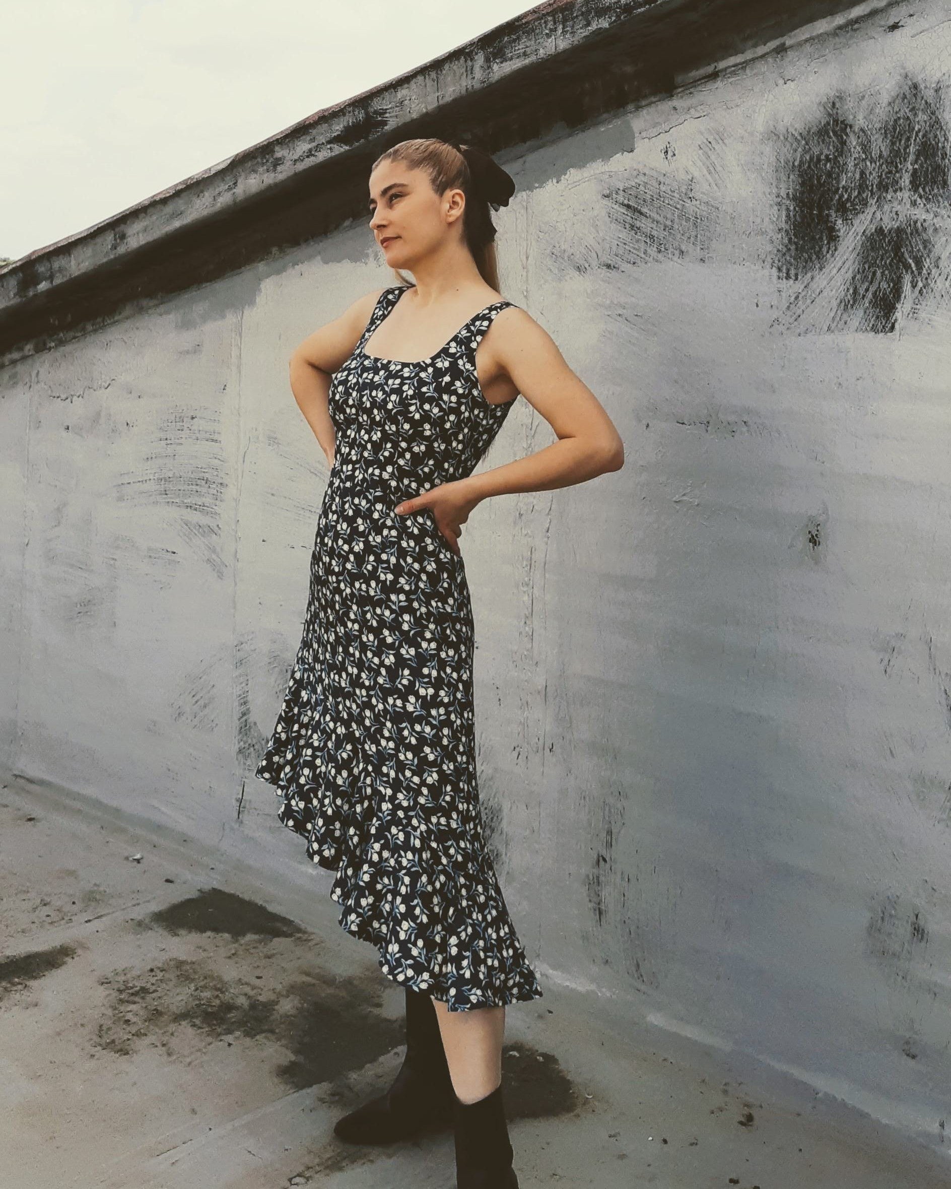 A woman with a ponytail posing in a sleeveless patterned dress.