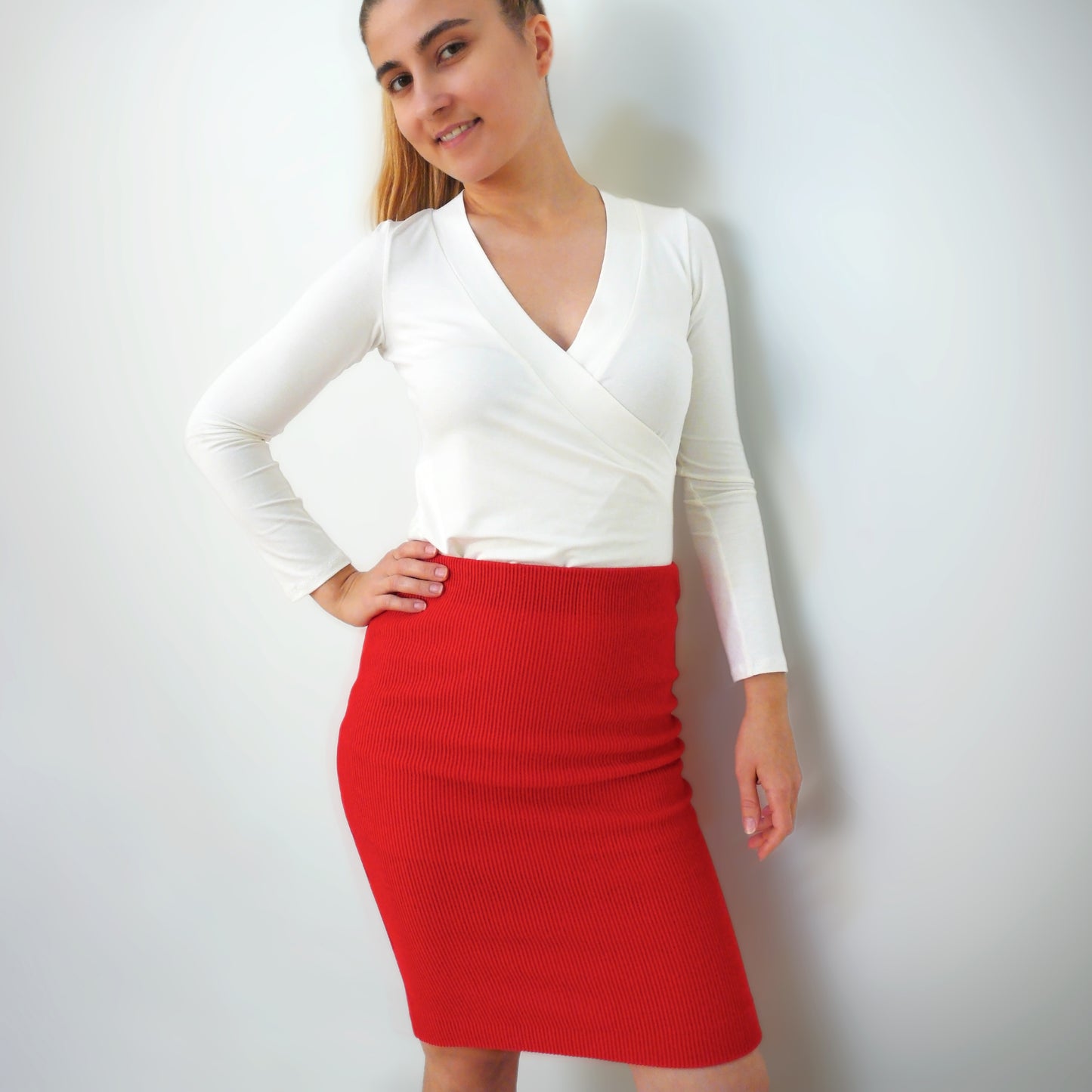 A woman posing in a red bodycon skirt and a long-sleeved, crossed-front top.