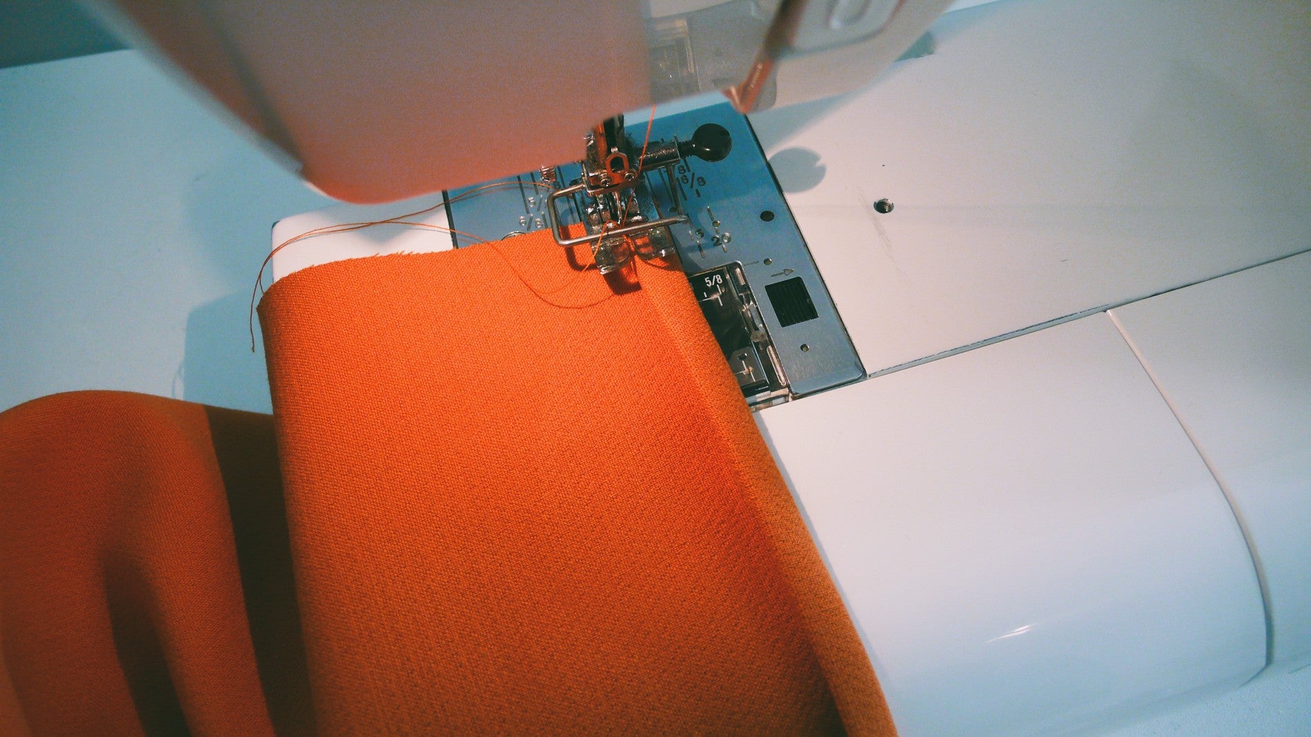 Orange fabric being sewn on a sewing machine