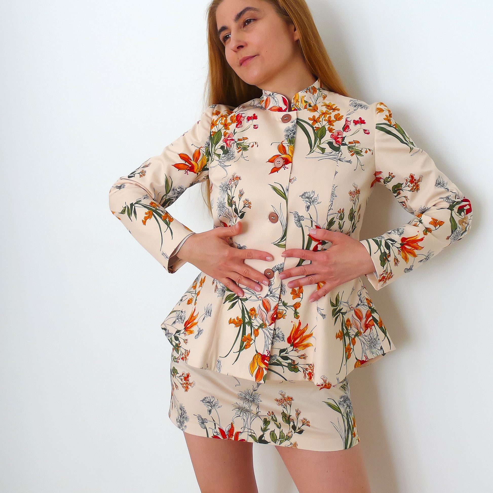 A woman is striking a pose in a floral peplum blazer and a corresponding mini skirt.